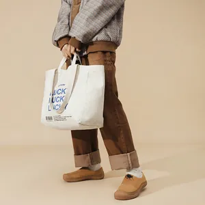 Dettaglio della borsa tote in tela crema con stampa Lucky blu su un outfit retrò
