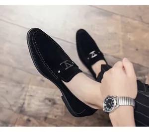 Detalle de mocasines de ante negro con hebilla metálica y costuras sobre suelo de madera