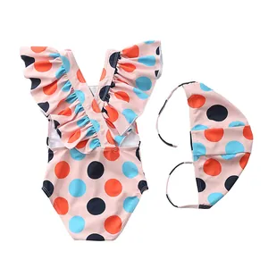 Detailed flat lay of a pink polka dot toddler swimsuit with ruffled collar and swim cap