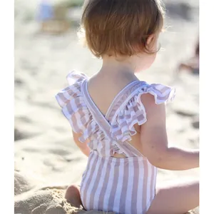 Girl's striped one-piece swimsuit with ruffled trim and cross-back straps on the beach