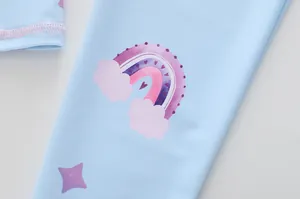 Détail du tissu bleu de maillot de bain enfant avec motif imprimé arc-en-ciel et nuages
