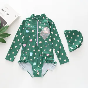 Flat-lay of green long-sleeve kids swimsuit with unicorn print and matching swim cap