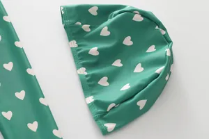 Close-up of green kids swimsuit fabric with white heart pattern and elastic swim cap