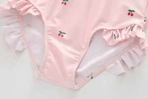 Close-up of pink girls swimwear featuring cherry prints and double-layered ruffle leg openings