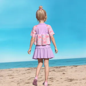 Outdoor shot of a girl wearing a pink and purple float vest with a matching pleated swim skirt