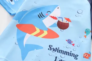 Dettaglio del costume da bagno per bambino con squalo surfista e scritta Swimming Lover