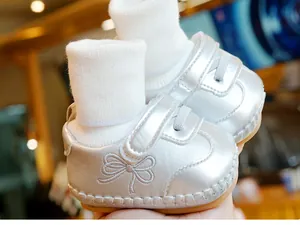 Detail van zilveren babyloopschoenen met geborduurde strik en geribbelde sokmanchetten
