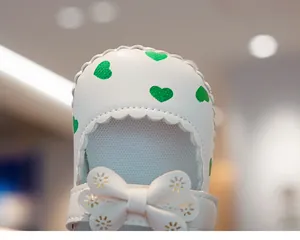 Detailed view of white baby walking shoes with green hearts and laser-cut floral bow