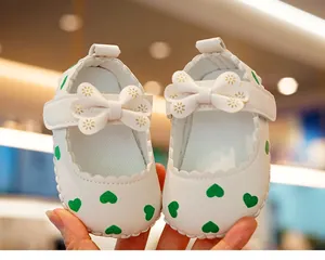 Detail of white baby shoes with green hearts, soft bow and secure velcro strap