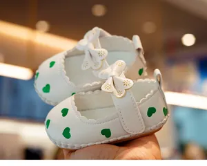 Close-up of white leather baby Mary Jane shoes with green heart pattern and bow detail