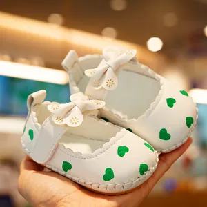 Soft-soled white Mary Jane baby shoes with green heart print and bow detail for infants