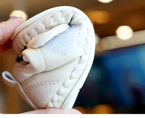 Macro detail of cream baby shoes showing flexible soft sole and hand-stitched leather texture