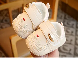 Detailed close-up of baby walking shoes featuring red floral embroidery and lace trim