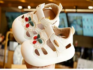 Close-up of white baby sandals with red cherry embroidery and protective closed-toe design