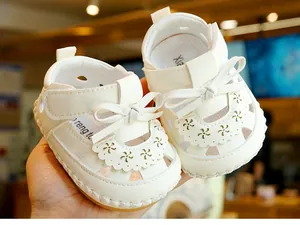 Close-up of white baby summer sandals with bow decoration and laser-cut petal details