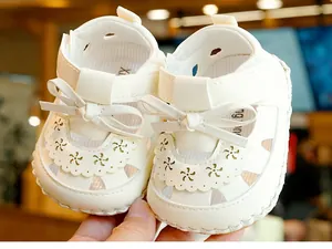 Detail of cream baby sandal with decorative bow, floral cutouts and velcro strap