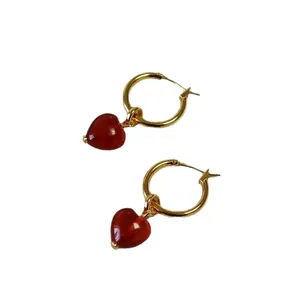 Elegant gold hoop earrings with translucent red heart pendants in a minimalist style