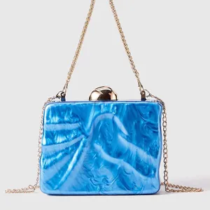 Detail of blue marble acrylic clutch bag featuring a gold spherical clasp and chain strap
