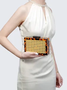Close-up of a rectangular acrylic evening clutch with wicker panels held by a model