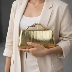 Close-up of golden evening clutch with wavy metal handle and textured leather finish