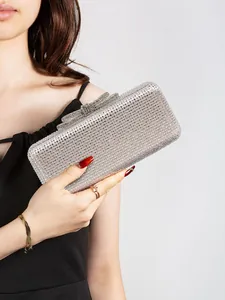 Detail of silver rhinestone evening bag with bow clasp held by a model in black dress