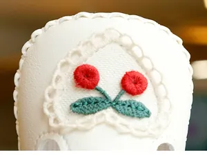 Détail de chaussure bébé avec broderie cerise et bordure en dentelle blanche