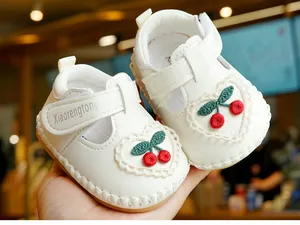 Détail de chaussure bébé blanche avec broderie cerise et motif cœur en dentelle fine