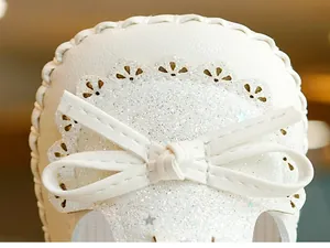 Close-up of white baby girl walker shoe with sequins, bow, and laser-cut wave edges