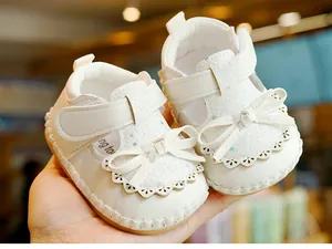 Close-up of white baby girl sandals with sequins, bow detail and lace trim