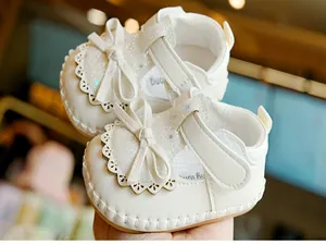 Detailed close-up of white baby girl shoes with glitter bow and laser-cut lace trim