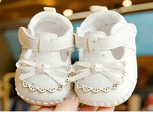 Close-up of white baby walker shoes featuring silver glitter toes and decorative bows