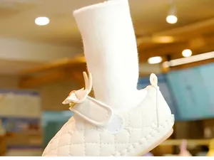 Detailed macro view of white quilted baby walker shoes with velcro straps and pink bows
