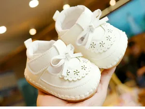 Detail of white infant walking shoes featuring laser-cut floral patterns and bow accents