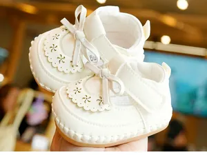 Close-up of white Mary Jane baby shoes with laser-cut hollow lace and bow detail