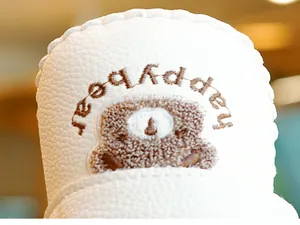 Detail eines weichen weißen Leder-Babyschuhs mit Happy Bear-Stickerei und Plüschtextur