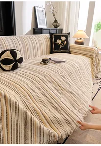 Detail of cream striped sofa throw cover with soft woven texture and decorative fringe edge
