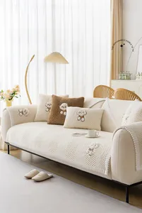 Detail of cream sofa cover with V-texture, pom-pom lace, and dog embroidery