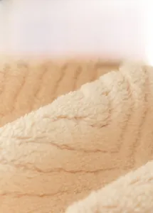 Close-up of beige plush sofa cushion fabric featuring wavy texture and soft angora finish