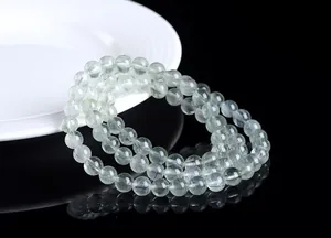 Detalle de pulsera multicapa de cuarzo rutilado verde sobre fondo de espejo negro