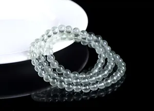 Detalle de cuentas de cuarzo rutilado verde translúcido sobre una base reflectante mínima