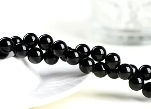 Macro shot of high-polish black tourmaline beads with reflective mirror finish on white tray
