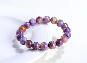 Gros plan de perles de charoïte naturelle violette sur une assiette blanche minimaliste