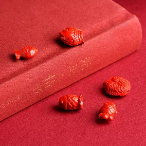 Detailed red cinnabar fish beads for DIY jewelry making on a festive red background