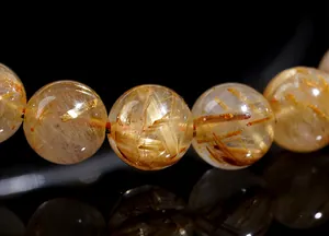 Macro shot of natural yellow rutilated quartz beads with golden needles on black surface