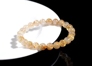Macro shot of natural rutilated quartz beads with golden needles on a white ceramic plate
