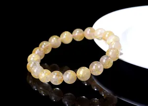 Macro detail of natural rutilated quartz bracelet with golden needle inclusions on black surface