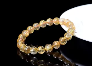 Macro shot of gold rutilated quartz beaded bracelet with needles on black background