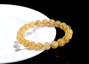 Close-up of golden rutilated quartz crystal beaded bracelet on white ceramic plate