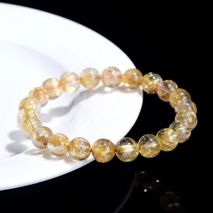 Natural gold rutilated quartz bead bracelet with golden needle-like inclusions on white plate