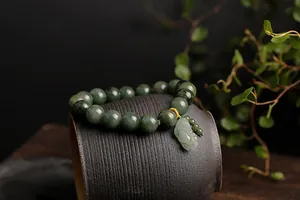 Macro detail of natural dark green jade beads and light green PiXiu charm on a ceramic bowl